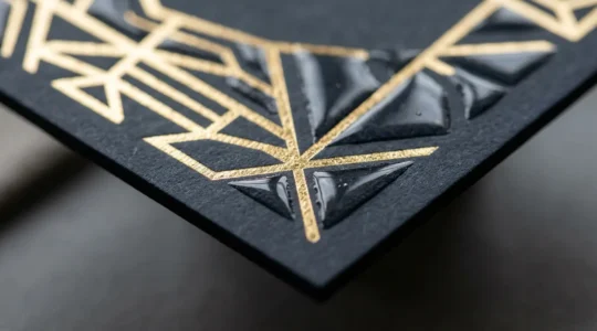 Détail macro d'une finition premium combinant dorure et vernis gonflant sur carte de visite haut de gamme