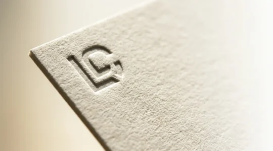 Carte de visite minimaliste sur papier épais texturé avec un seul logo embossé entouré d'espace blanc