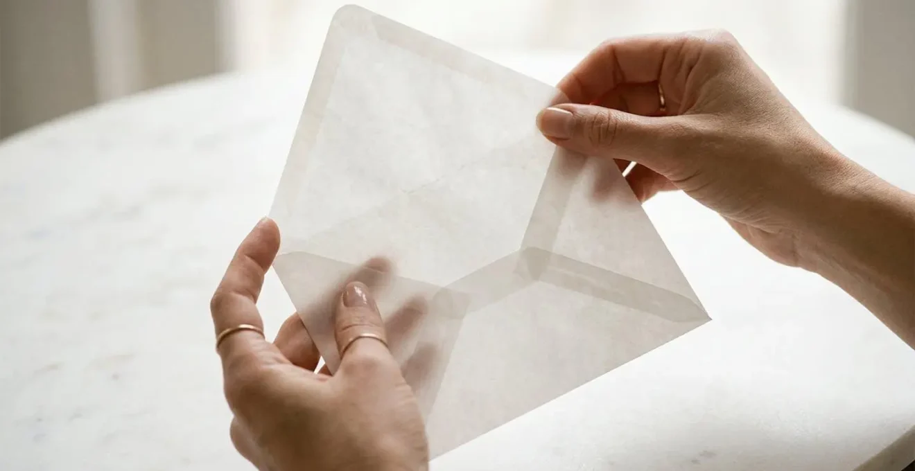 Mains délicates ouvrant une enveloppe en papier calque translucide, capturant l'instant du dévoilement